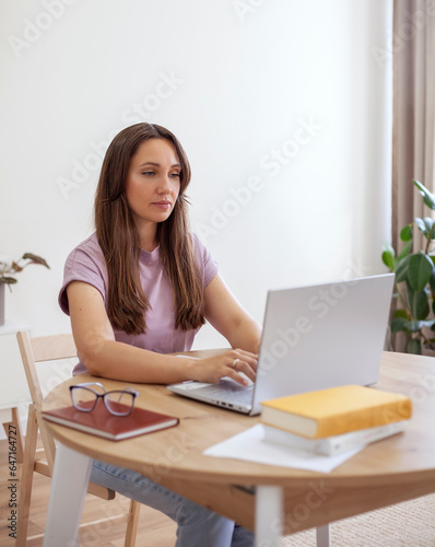 Attractive young woman sitting at a table and working on a laptop