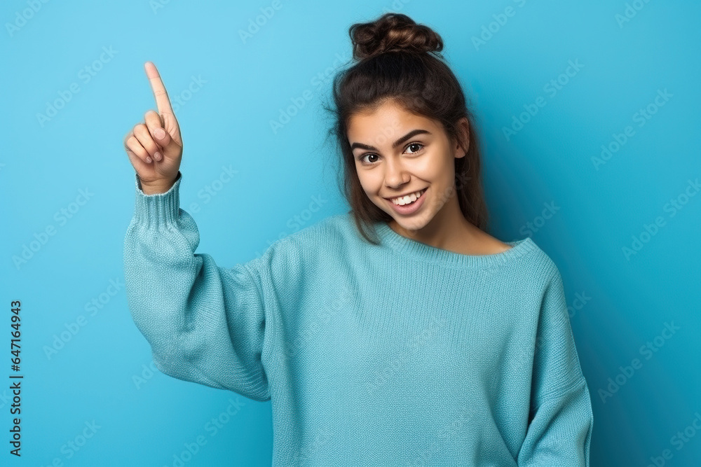 A 17 years old girl on a blue background gesticulates with her index finger, copy space