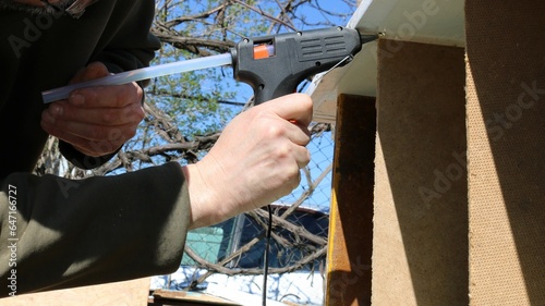 working with a glue gun when creating a wooden structure, gluing plywood and wood using construction glue from a gun with a long tube, a craftsman gluing fragments of a household device photo