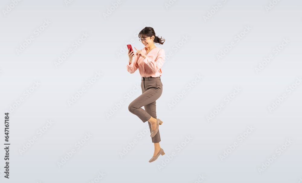 スマホを使いながらジャンプするミドル女性（切り抜き背景透過PNGも販売しております。作成者リンクから「PNG」で検索してください）