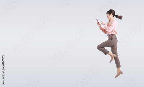 スマホを使いながらジャンプするミドル女性（切り抜き背景透過PNGも販売しております。作成者リンクから「PNG」で検索してください） © metamorworks