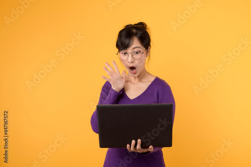 Young surprised woman of Asian ethnicity 30s wear purple shirt with glasses using laptop pc computer isolated on plain yellow studio background. Surprise news from online electronic mail concept.
