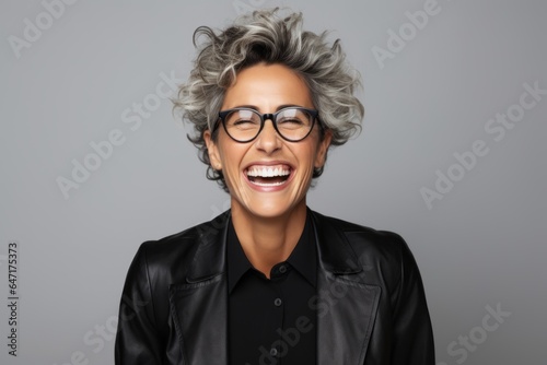 Portrait of a happy middle-aged woman in eyeglasses laughing against grey background