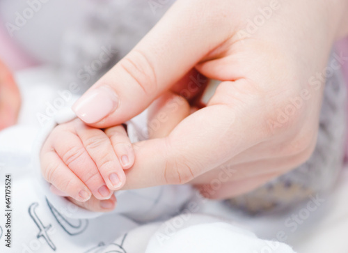 Newborn baby touching his mother hand. Mother uses her hand to hold her baby's tiny hand to make him feeling her love, warm and secure. Concept of child care, feeling safe, parent love.