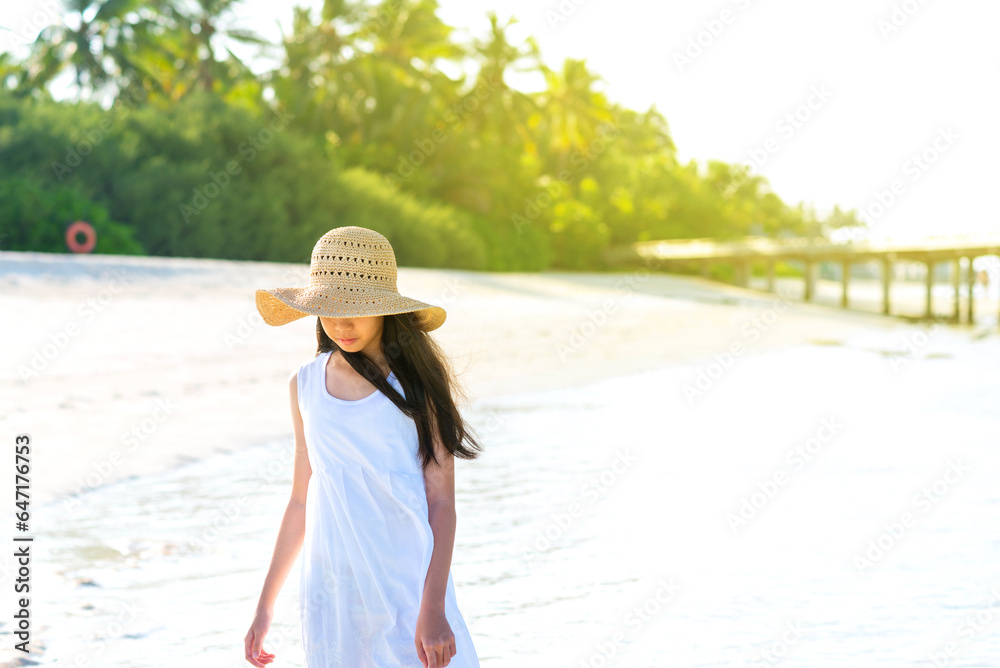 Portrait of young Asian girl walking on white sand beach with mangrove tree. Teenager girl wearing sun straw hat, white dress enjoy vacation. Outdoor summer travelling concept, copy space.