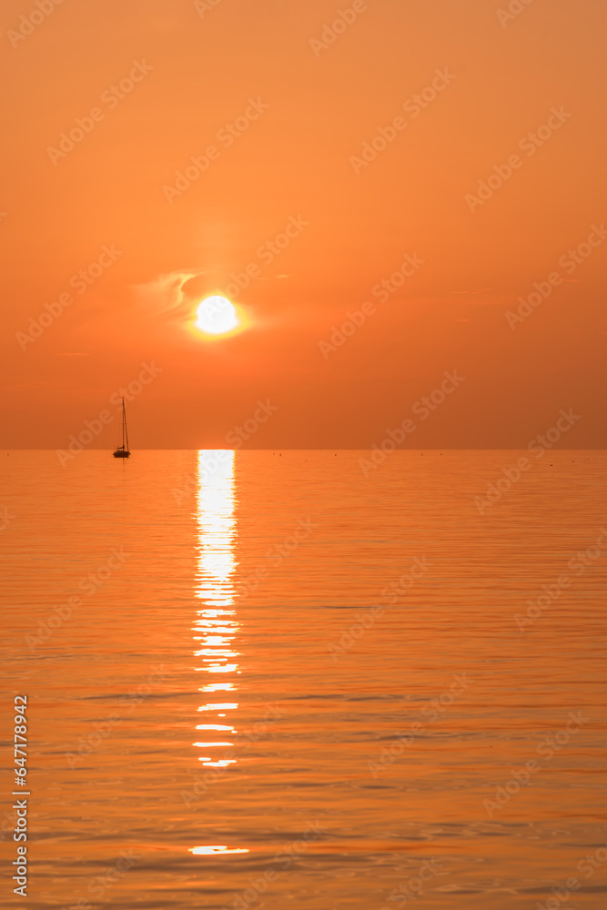 View of a sailboat sailing on a lake during sunset with an orange sky.