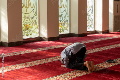an old asian muslim man is praying in a mosque with beautiful islamic mosaic glass