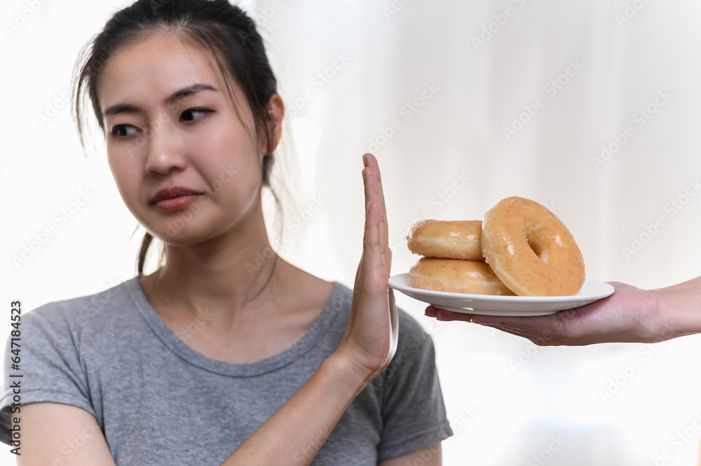 Dieting or good health concept. Young woman rejecting junk food or unhealthy food such donut because concern about health sickness and body weight. Young woman self care food control diet concept. Dieting or good health concept. Young woman rejecting junk food or unhealthy food such donut because concern about health sickness and body weight. Young woman self care food control diet concept.