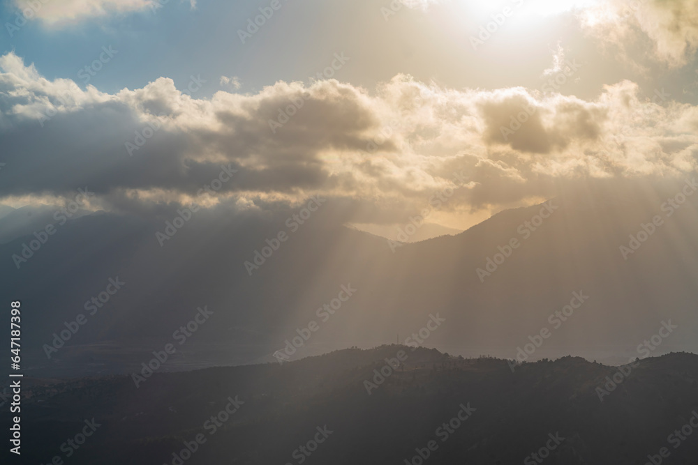 The sun rising behind the mountains and the rays of light leaking through the clouds The sun rising behind the mountains and the rays of light leaking through the clouds