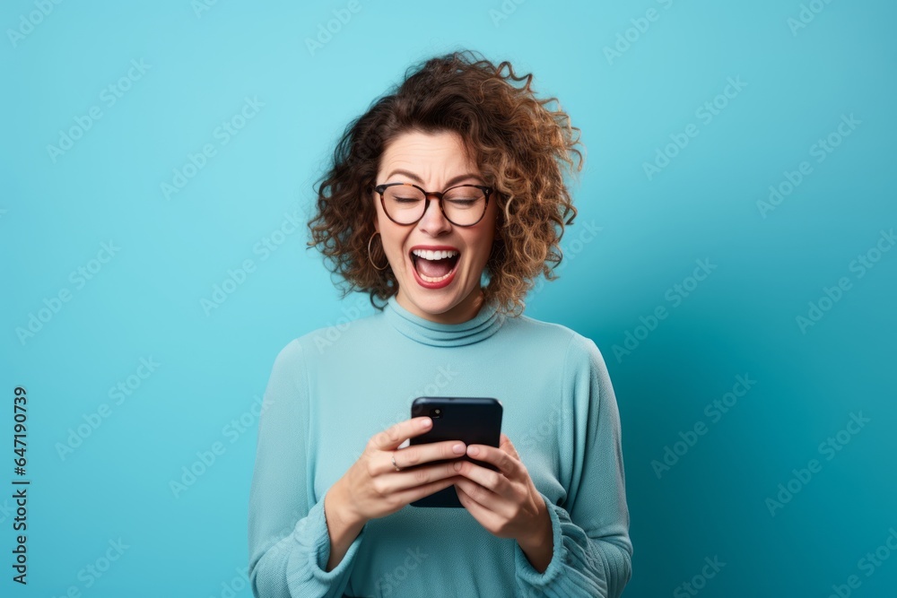 Portrait of a young woman with curly hair using mobile phone on blue background - obrazy, fototapety, plakaty 