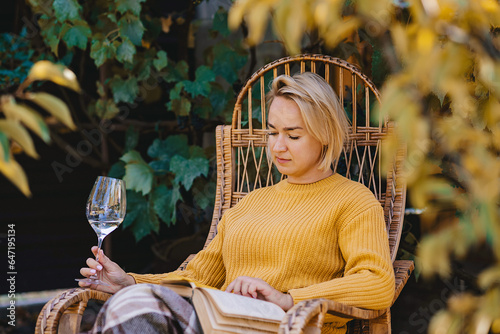 woman in sweater reads a book and drinking wine in terrace