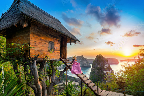 Young girl on steps of house on tree at sunrise in Nusa Penida island, Bali in Indonesia. photo