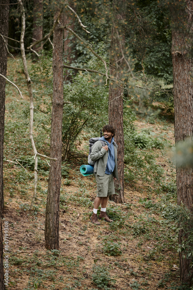 happy indian backpacker with curly hair walking in forest, natural location, hiker with backpack happy indian backpacker with curly hair walking in forest, natural location, hiker with backpack