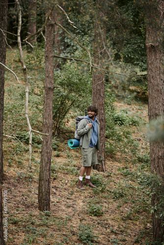 happy indian backpacker with curly hair walking in forest, natural location, hiker with backpack