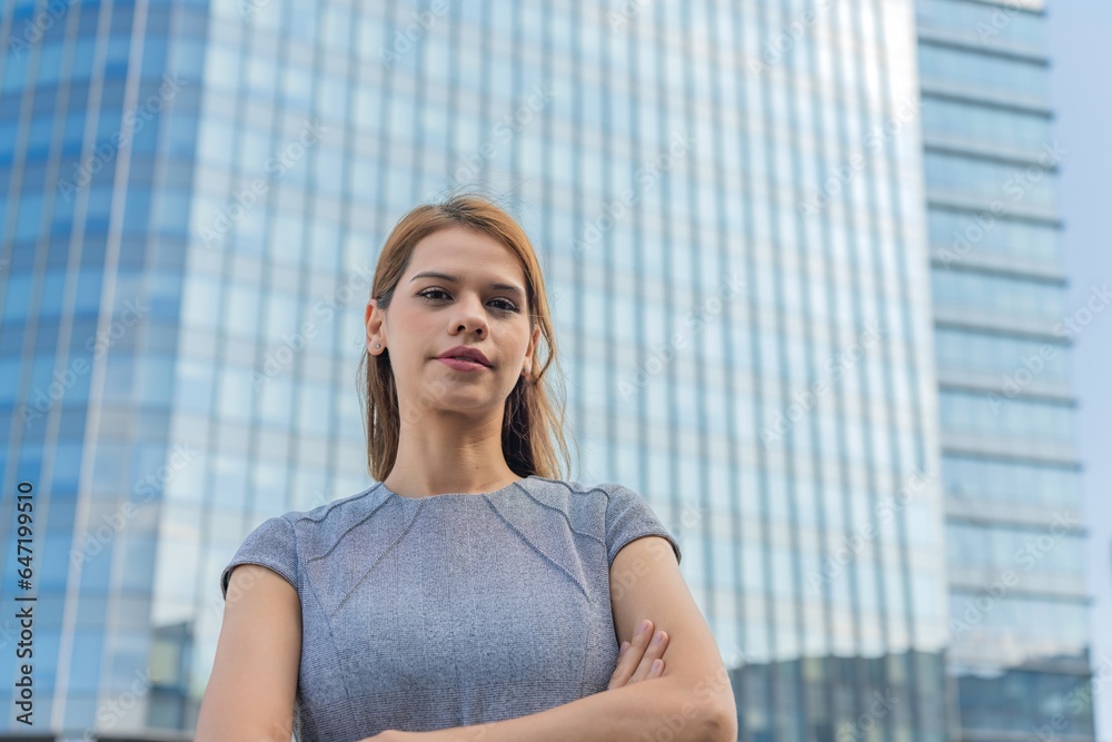 Portrait of a young and successful white caucasian business woman standing in front of a modern cityscape of office buildings