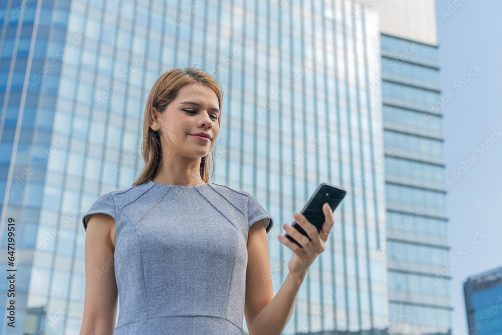 Business on the move. Young caucasian white businesswoman using smartphone while commuting in a central business district against a background of modern skyscraper cityscape. Business on the move. Young caucasian white businesswoman using smartphone while commuting in a central business district against a background of modern skyscraper cityscape.