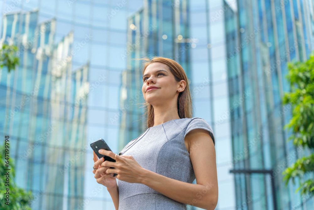 Business on the move. Young caucasian white businesswoman using smartphone while commuting in a central business district against a background of modern skyscraper cityscape. Business on the move. Young caucasian white businesswoman using smartphone while commuting in a central business district against a background of modern skyscraper cityscape.