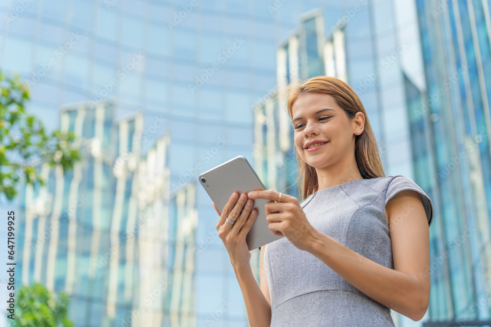 Business on the move. Digital banking on the go. Portrait of a young and successful white caucasian business woman using digital tablet standing in front of a modern cityscape of office buildings. 