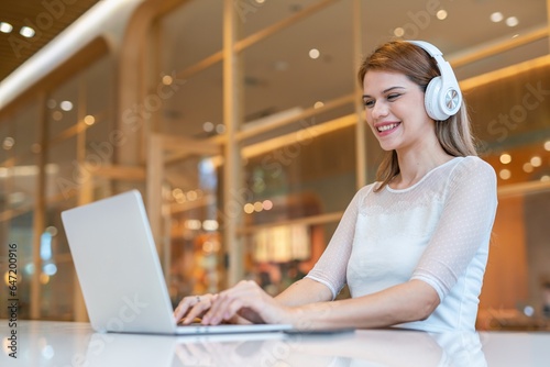 Young caucasian woman wearing headphone using laptop at a local cafe