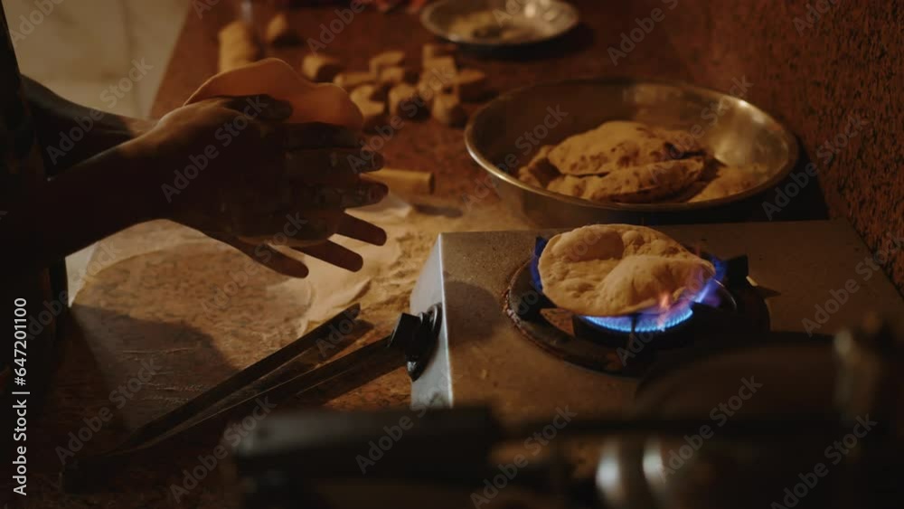 Cook sculpts and rolls wheat dough and cooks a traditional Indian dish chapati on an open fire on gas in the kitchen. Indian National Bread