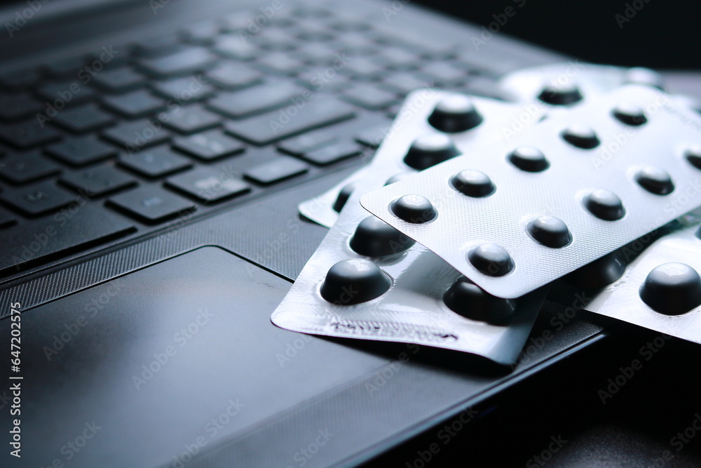 Antipyretic tablets in foil blister pack on a laptop keyboard selective focus - obrazy, fototapety, plakaty 