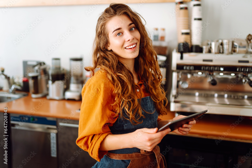 Smiling female barista takes an order from a panchette while standing at the bar counter in a coffee shop. Business concept. The concept of tenologies, takeaway food. Smiling female barista takes an order from a panchette while standing at the bar counter in a coffee shop. Business concept. The concept of tenologies, takeaway food.