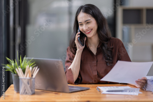 Cheerful business Asian woman freelancer making telephone call share good news about project working in office workplace, business finance concept. 