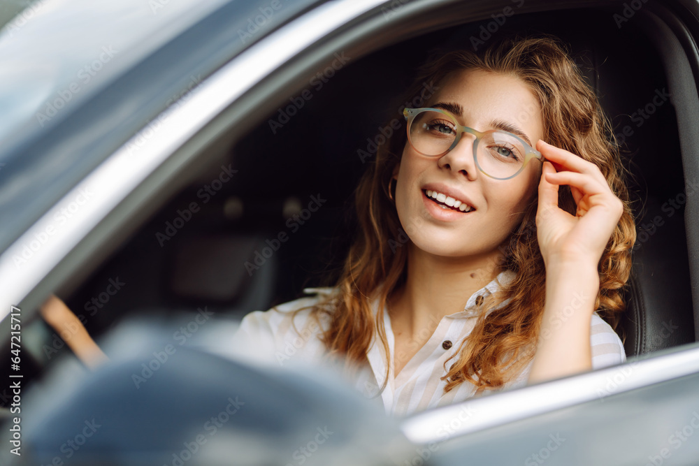Cute woman in casual clothes is sitting behind the wheel of a car. Traveler-driver. Concept of mode of transportation, travel.