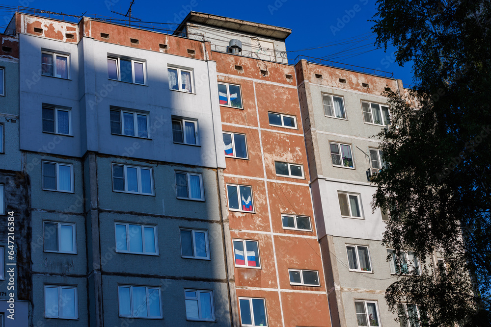 typical russian ugly high rise apartmant building with russian national flags in some windows at summer day.