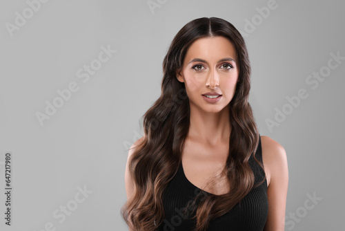Hair styling. Portrait of beautiful woman with wavy long hair on grey background, space for text