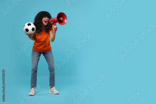 Happy fan with soccer ball using megaphone on light blue background, space for text