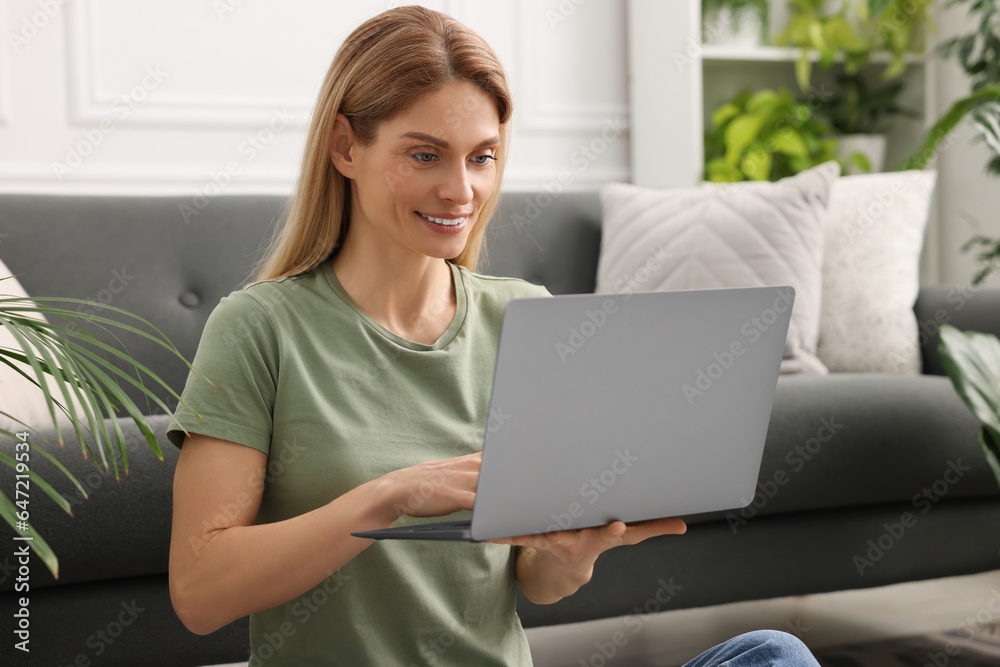 Woman using laptop in room with beautiful potted houseplants Woman using laptop in room with beautiful potted houseplants