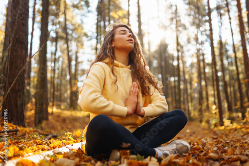 Young woman performs yoga exercises in the autumn forest, on fallen leaves. Lifestyle, meditation concept. Enjoying.