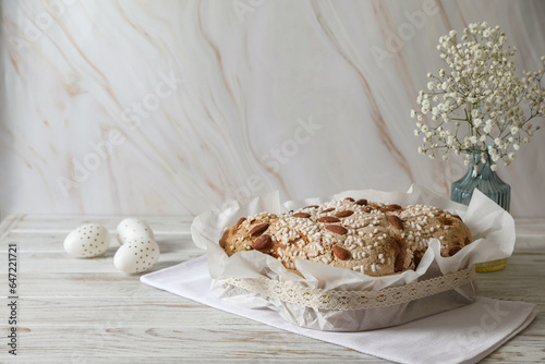 Delicious Italian Easter dove cake (traditional Colomba di Pasqua), decorated eggs and flowers on white wooden table. Space for text