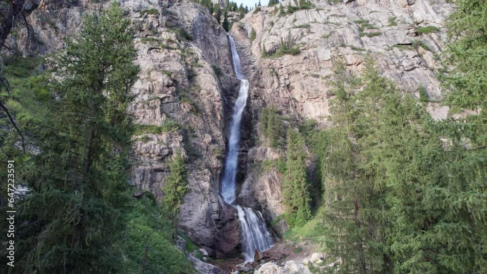 A high waterfall cascades in a mountain gorge. Coniferous trees, Christmas trees and grass grow. The river runs. Hiking trails. Top view from a drone. Sunset. Burkhan Bulak Waterfall, Kazakhstan A high waterfall cascades in a mountain gorge. Coniferous trees, Christmas trees and grass grow. The river runs. Hiking trails. Top view from a drone. Sunset. Burkhan Bulak Waterfall, Kazakhstan