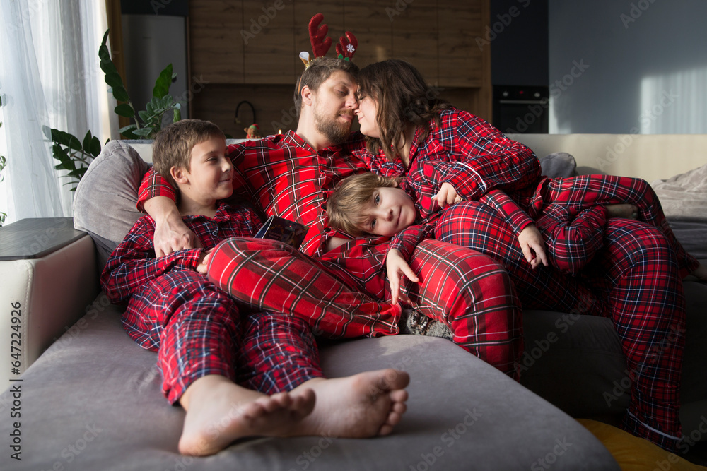 family mom, dad and two children brothers in red pajamas on Christmas morning at home.