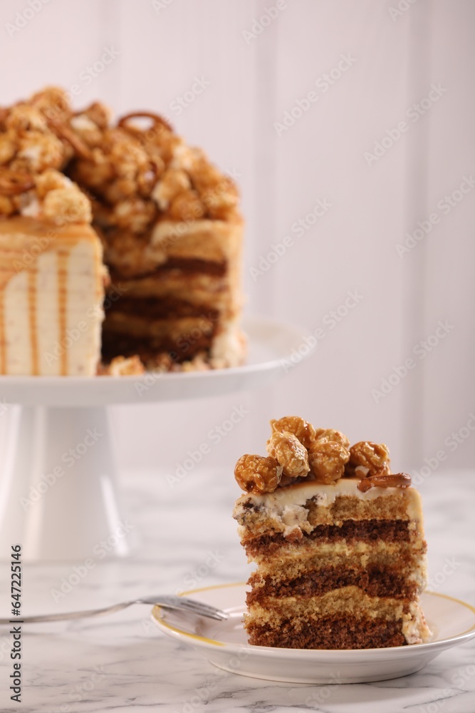 Piece of caramel drip cake decorated with popcorn and pretzels on white marble table Piece of caramel drip cake decorated with popcorn and pretzels on white marble table