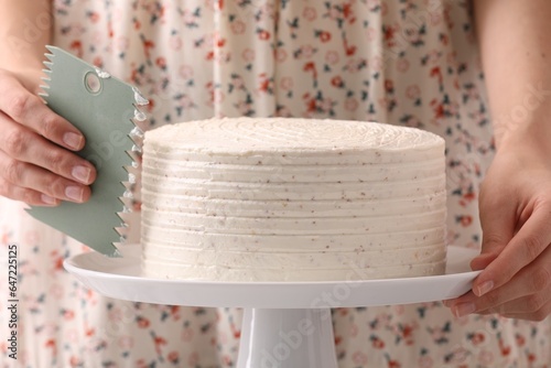 Woman using scraper to decorate cake, closeup photo