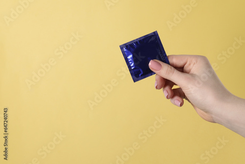 Woman holding condom on pale yellow background, closeup. Space for text