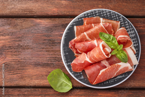 Plate with rolled slices of delicious jamon and basil on wooden table, top view. Space for text