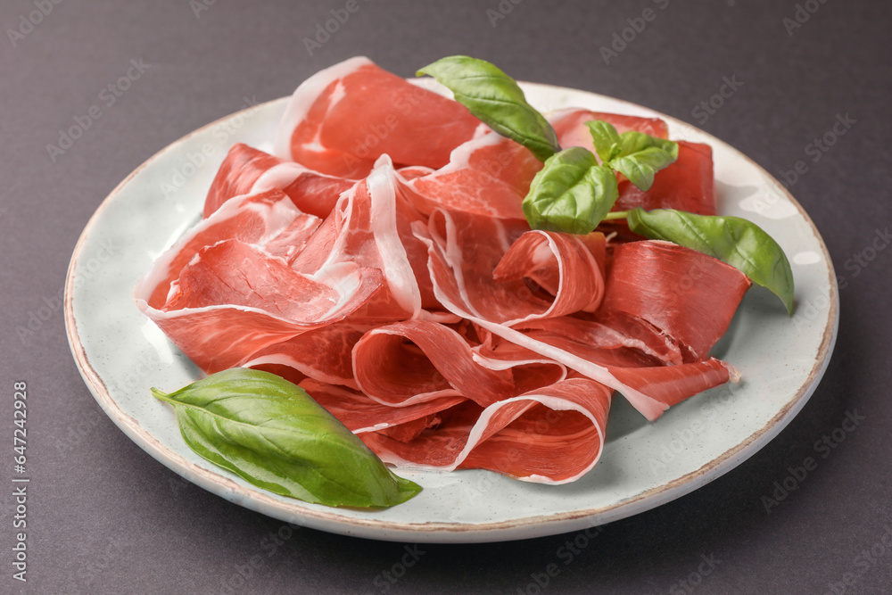Slices of tasty cured ham and basil on grey background, closeup