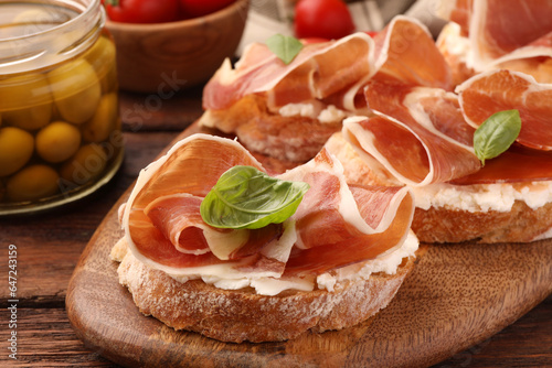 Board of tasty sandwiches with cured ham, basil and cream cheese on wooden table, closeup