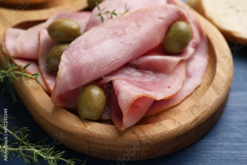 Slices of delicious ham with olives and thyme on blue wooden table, closeup