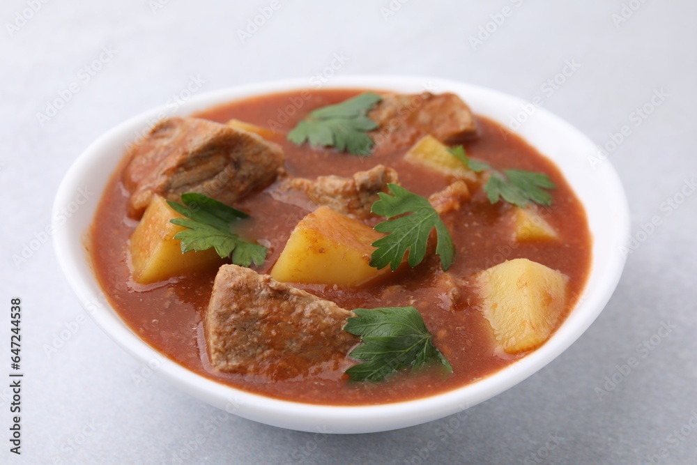 Delicious goulash in bowl on light grey table, closeup Delicious goulash in bowl on light grey table, closeup