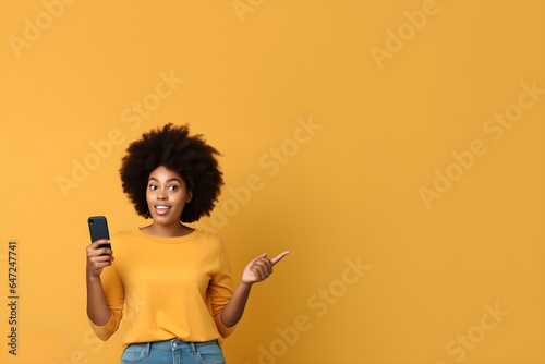 Young happy and excited black woman holding a cellphone and pointing at the background 
