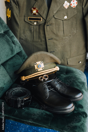 Golden rings, a cap, leather shoes, a belt, a uniform of a Ukrainian military groom with orders, awards close-up. Wedding photography, accessories, details. War in Ukraine.
