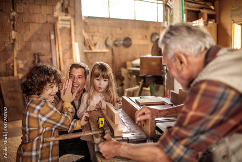 Grandfather carpenter teaching his son and grandchildren how to work with wood in a wood workshop