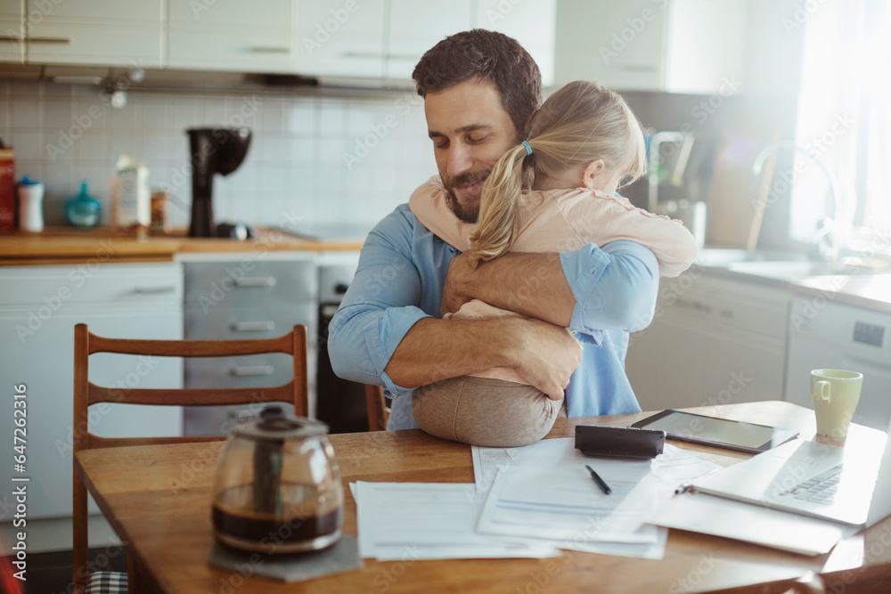Young single father finding hope in his daughters embrace while stressing over bills and home finances in the morning in the kitchen Young single father finding hope in his daughters embrace while stressing over bills and home finances in the morning in the kitchen