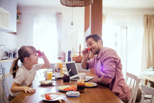 Young single father having fun and eating breakfast with his daughter in the kitchen