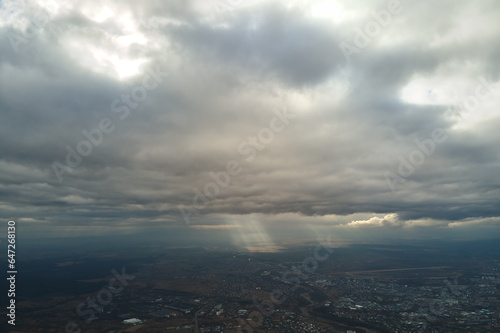 Aerial view from high altitude of distant city covered with puffy cumulus clouds forming before rainstorm in evening. Airplane point of view of cloudy landscape